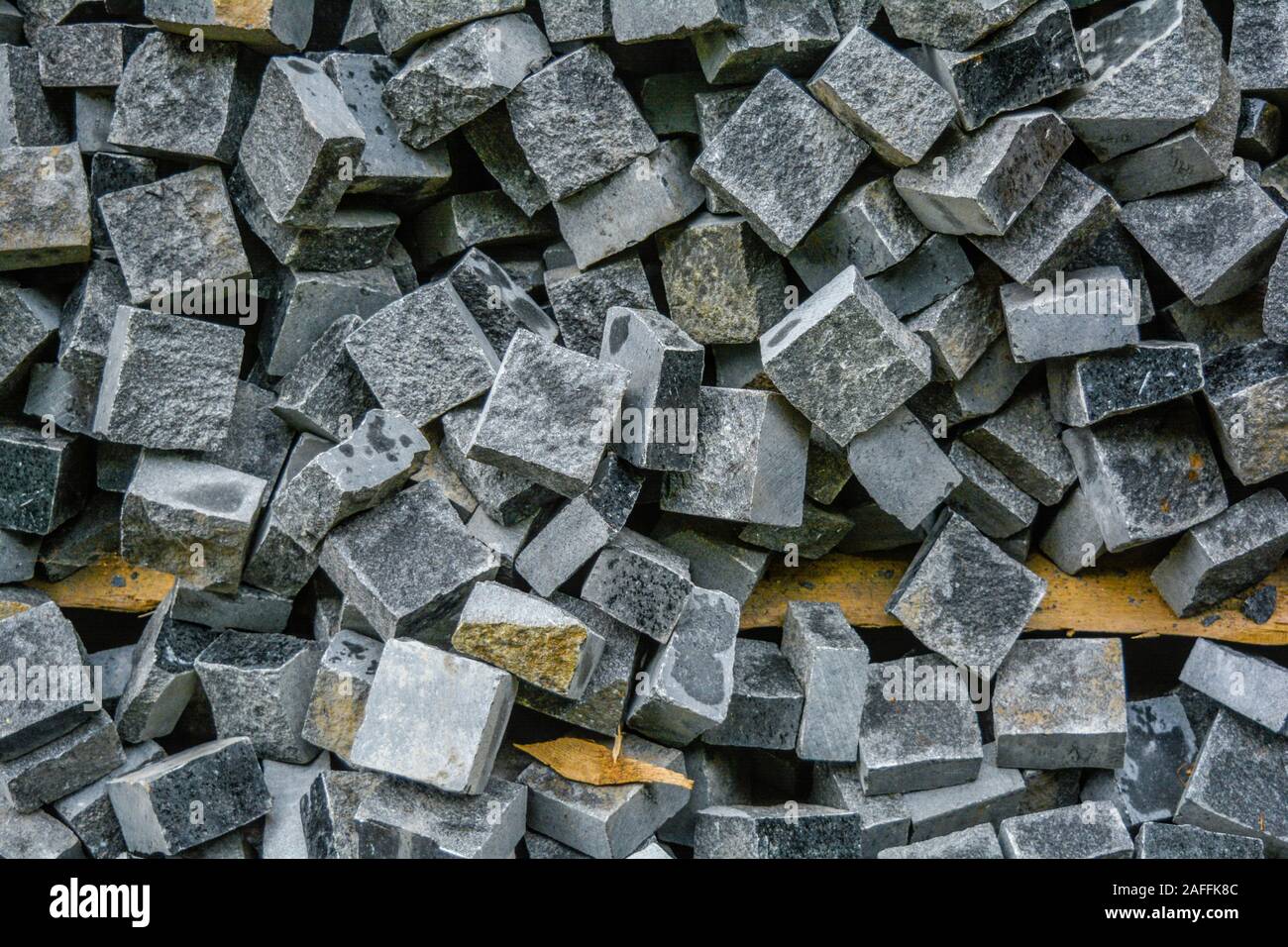Pila di nera pietra naturale cubi per rendere pavimento esterno di piastrelle. Cataste caotiche di rotture di piastrelle su strada. Costruzione sullo sfondo di un pasticcio bac geometrica Foto Stock