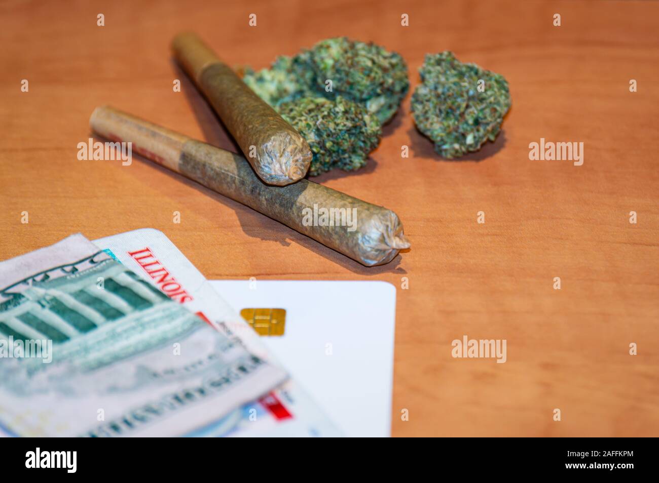 Ricreativo della cannabis legalizzazione in Illinois. Due giunti di marijuana sono visualizzate con un'Illinois ID card e denaro su un tavolo. Foto Stock