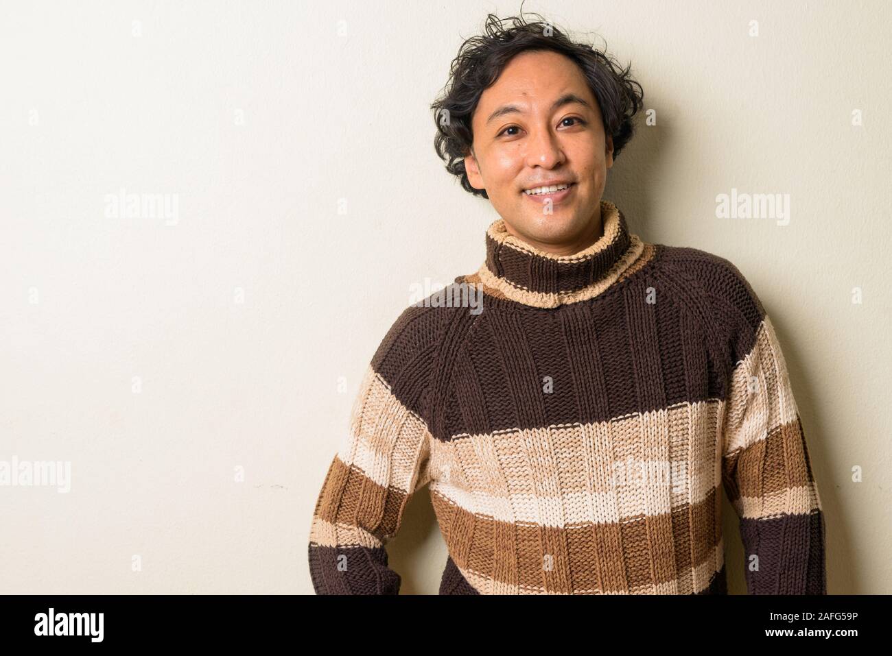 Ritratto di felice uomo giapponese con capelli ricci sorridente pronto per l'inverno Foto Stock
