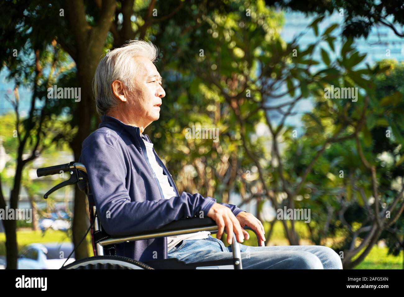 Vista laterale di asian senior uomo seduto nella sedia a rotelle all'aperto Foto Stock