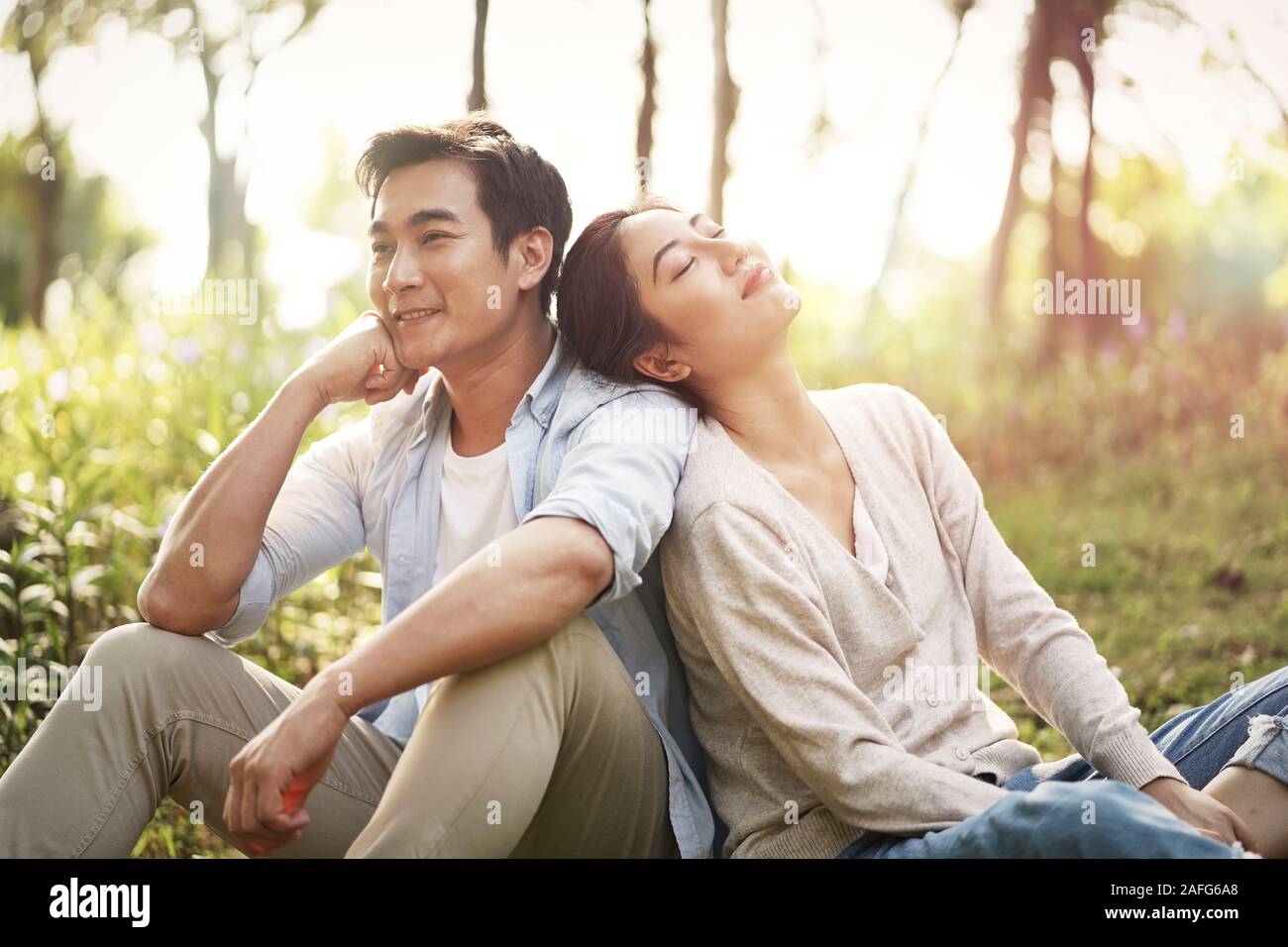 Bella felice giovani asiatici giovane seduto sull'erba a parlare in chat relax nel parco Foto Stock