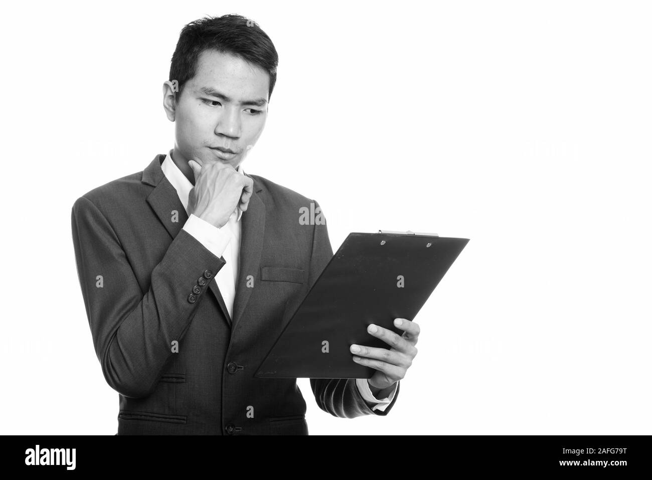 Studio shot del giovane imprenditore asiatici lettura sulla clipboard mentre pensando Foto Stock