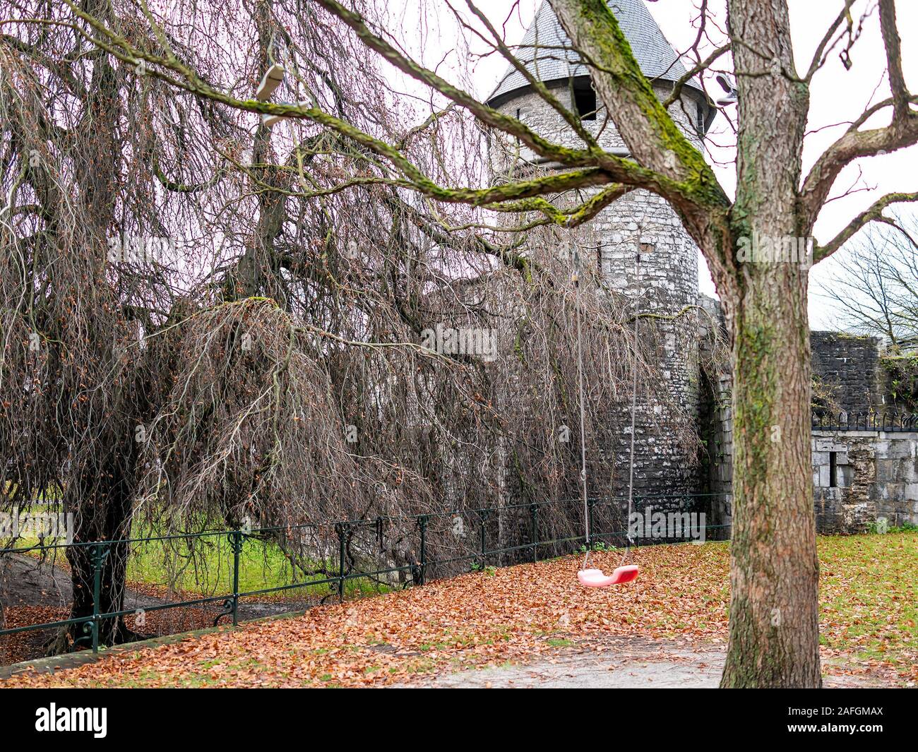 18 Childs swing di plastica appesi da un vecchio albero durante i mesi invernali con un antico borgo medioevale la costruzione di pietra in background Foto Stock