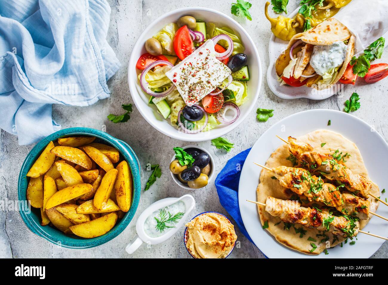 Piatto di laici cibo greco: insalata greca, pollo souvlaki, giroscopio e patate al forno su sfondo grigio, vista dall'alto. Gustate la cucina greca tradizionale concetto. Foto Stock