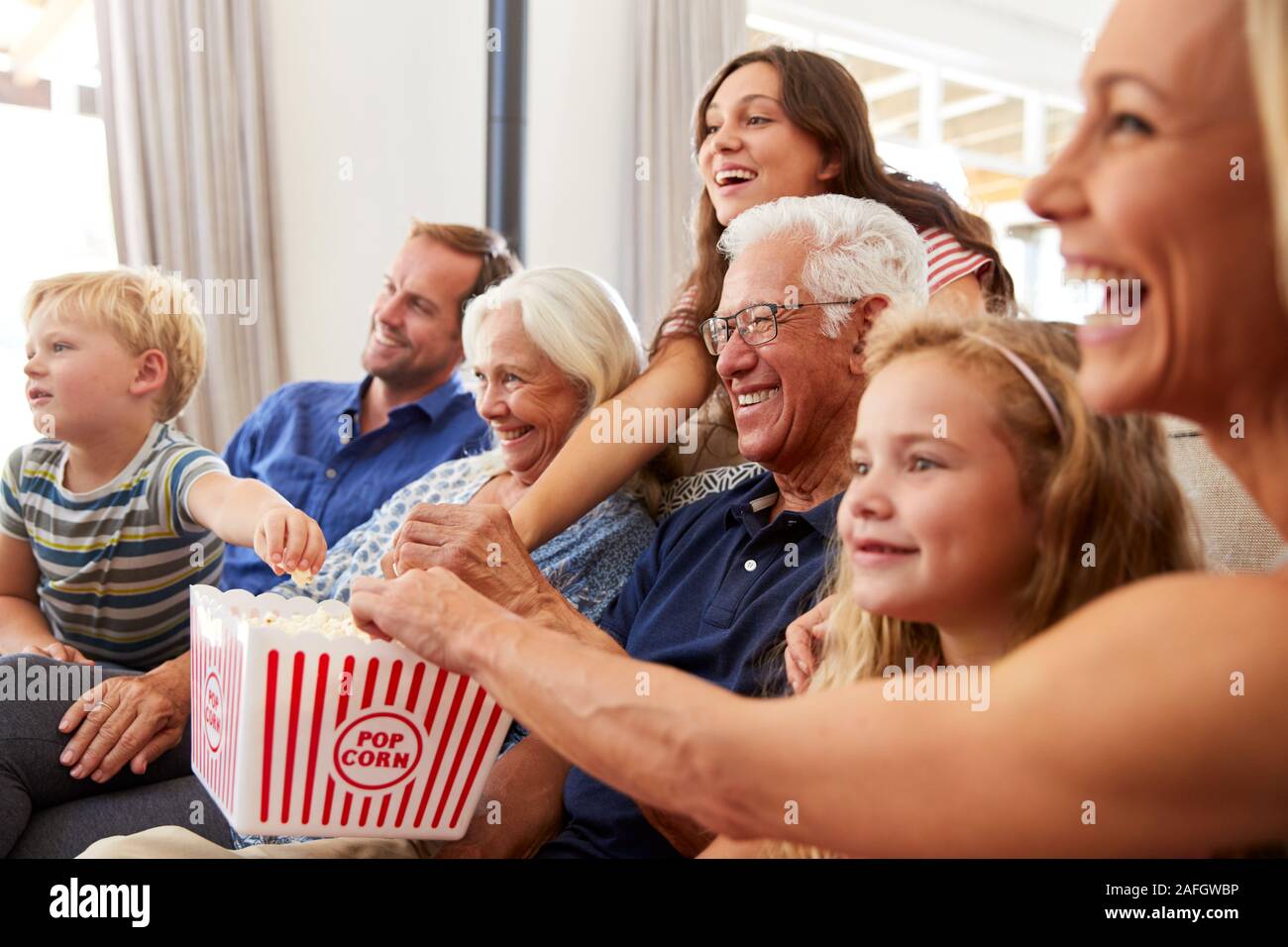 Famiglia Multi-Generation seduti sul divano di casa mangiare popcorn e guardare film insieme Foto Stock