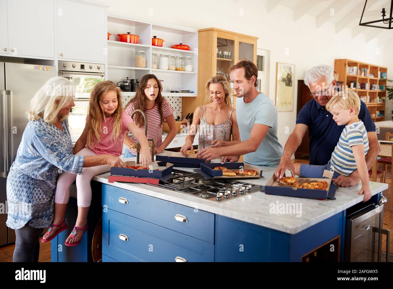 Multi generazione Famiglia intorno a Isola per cucina mangiare pizza da asporto insieme Foto Stock