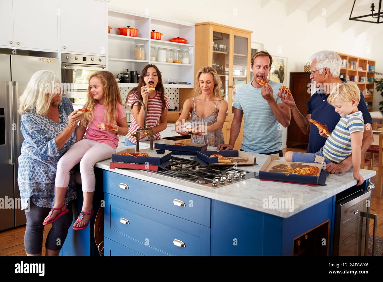 Multi generazione Famiglia intorno a Isola per cucina mangiare pizza da asporto insieme Foto Stock