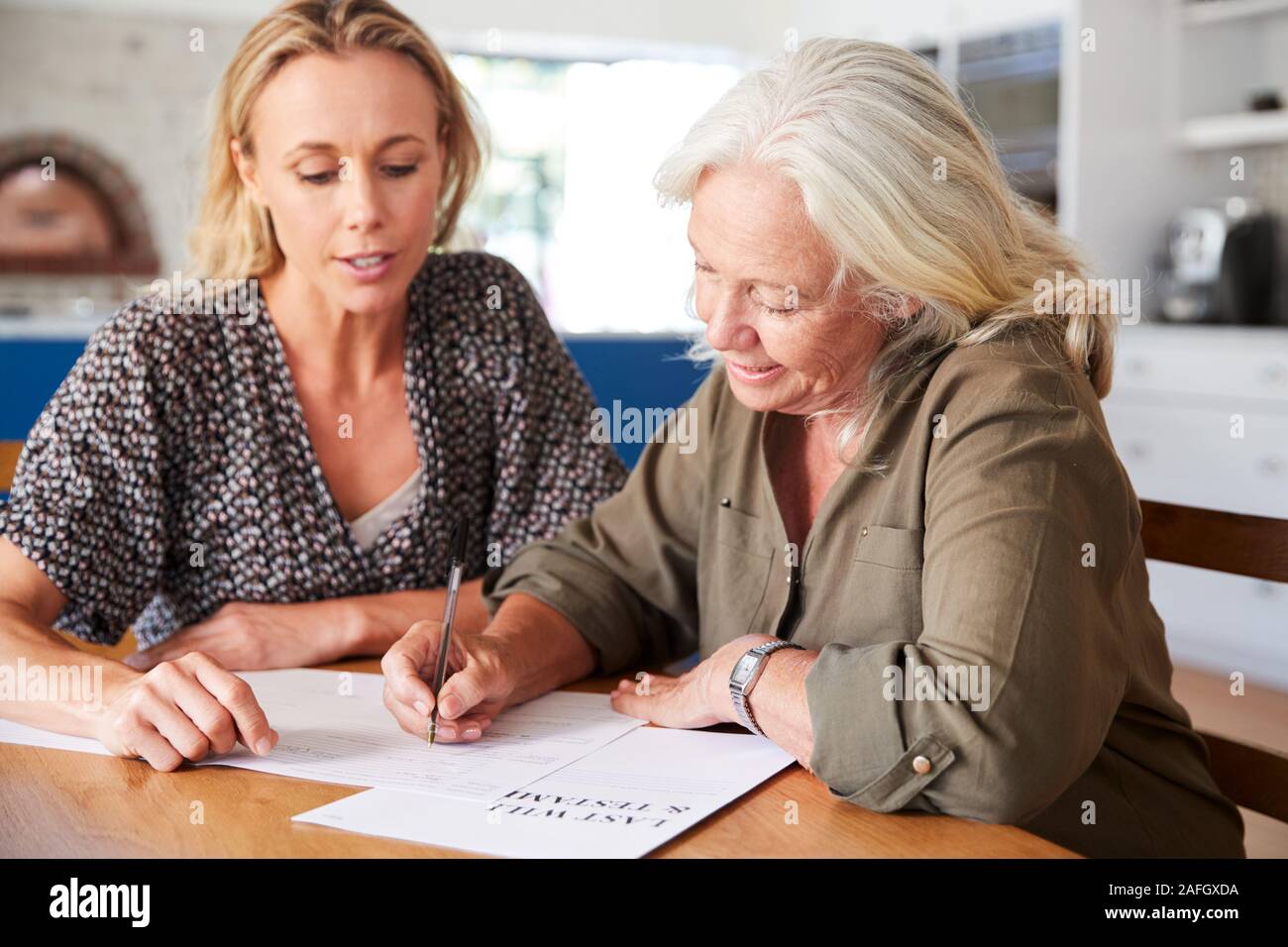 Amico femminile aiutando donna Senior per completare l'ultima volontà e testamento a casa Foto Stock