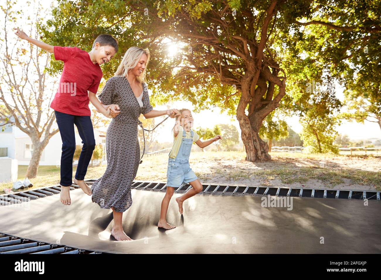 La madre a giocare con i bambini sul trampolino all'aperto in giardino Foto Stock
