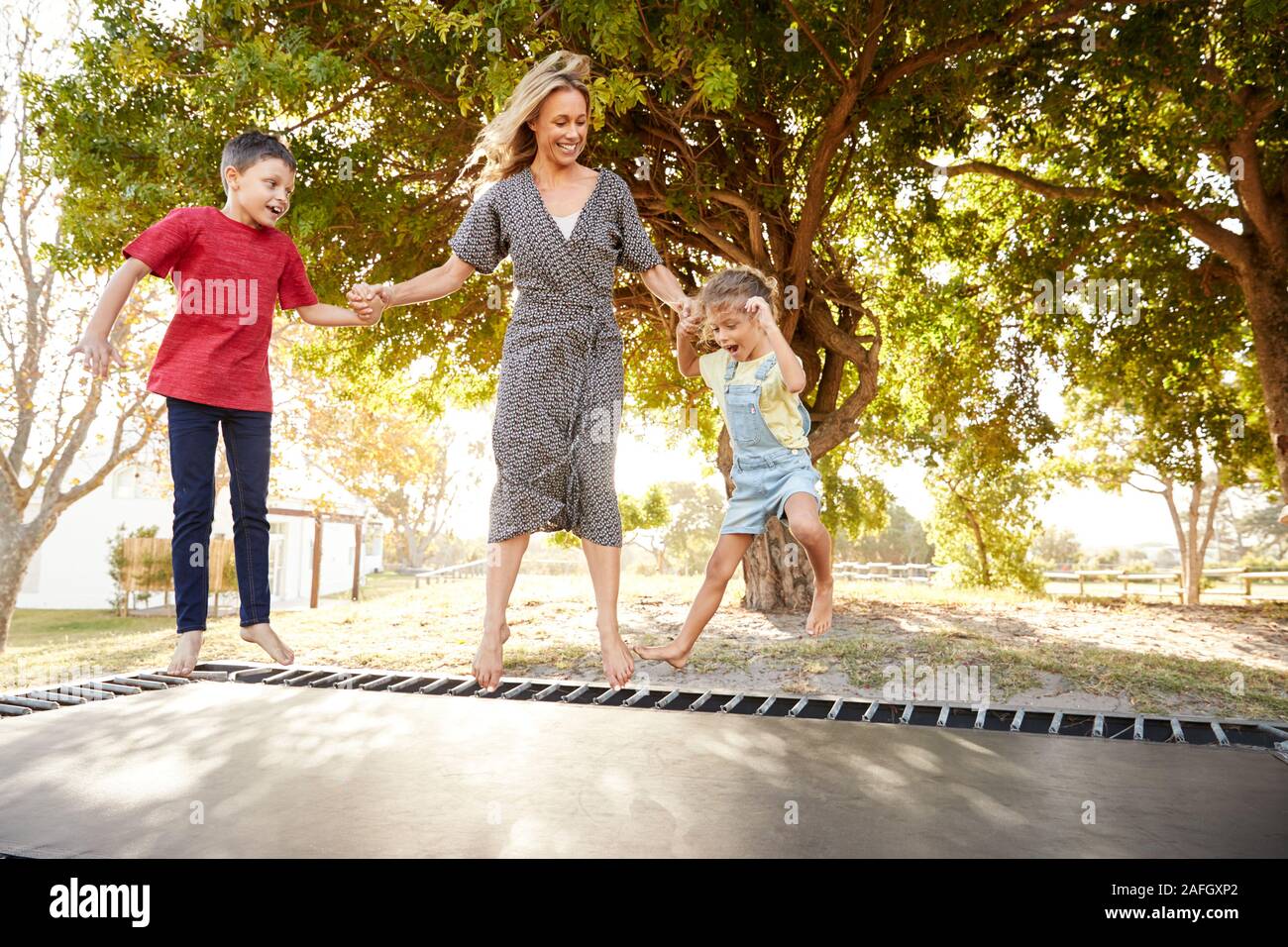 La madre a giocare con i bambini sul trampolino all'aperto in giardino Foto Stock