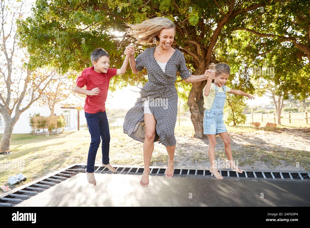 La madre a giocare con i bambini sul trampolino all'aperto in giardino Foto Stock