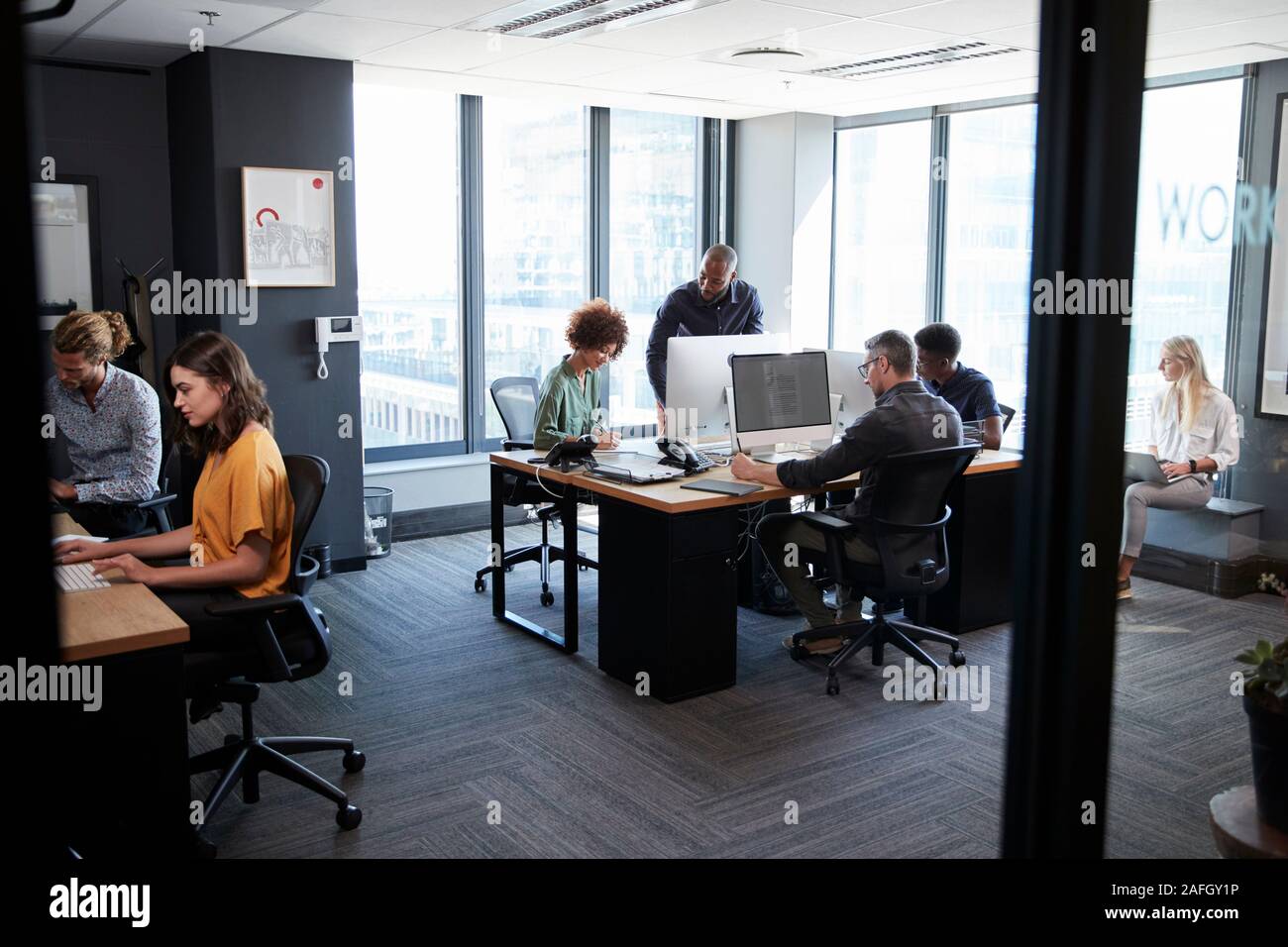I giovani creativi team lavorano insieme al computer in un ambiente informale e ufficio, visto dalla porta Foto Stock