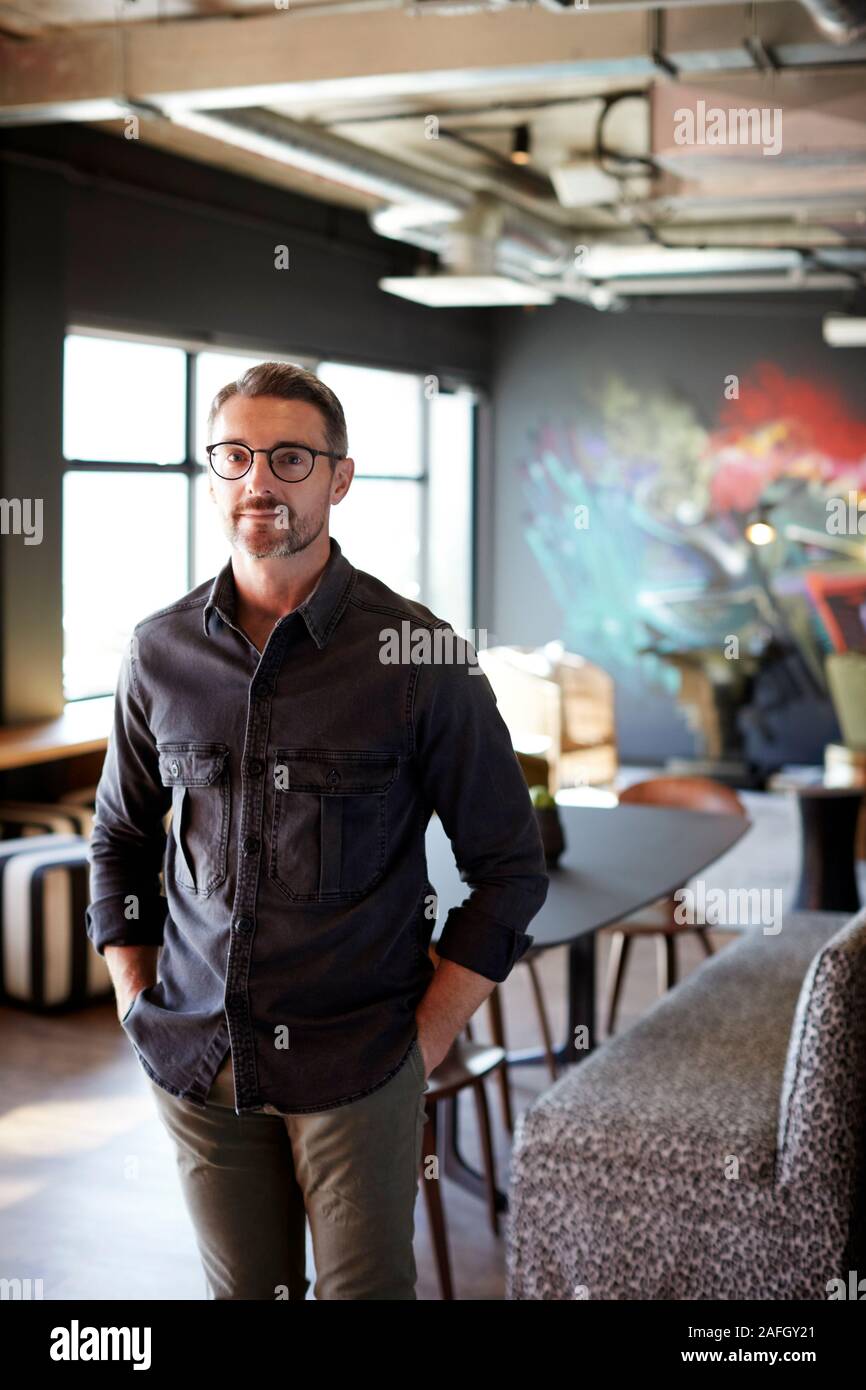 Di mezza età maschio bianco creative in piedi in ufficio informale area salotto guardando alla telecamera, verticale Foto Stock