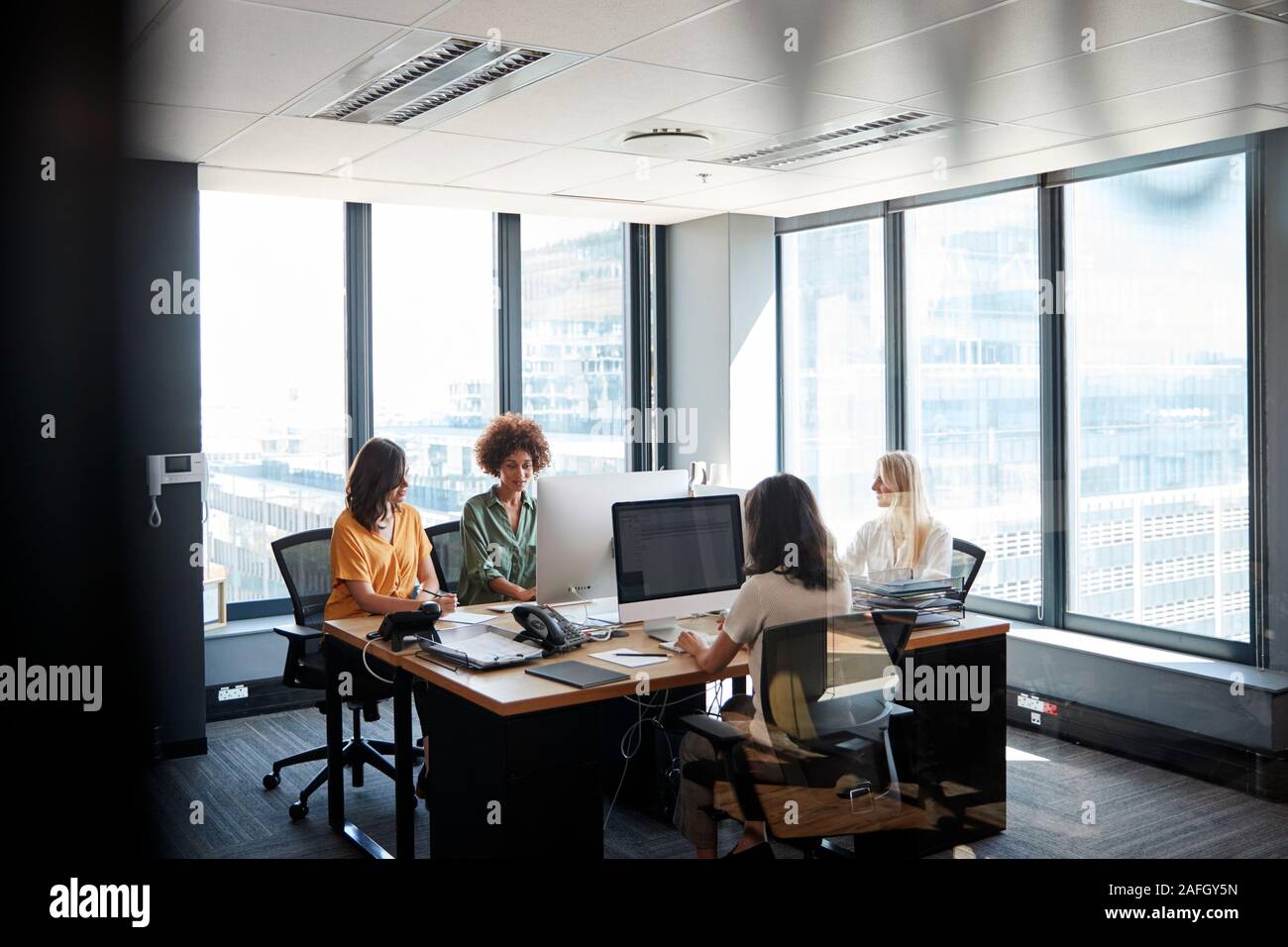 Quattro femmine colleghi creativi che lavorano insieme in un ufficio, visto attraverso la parete in vetro Foto Stock
