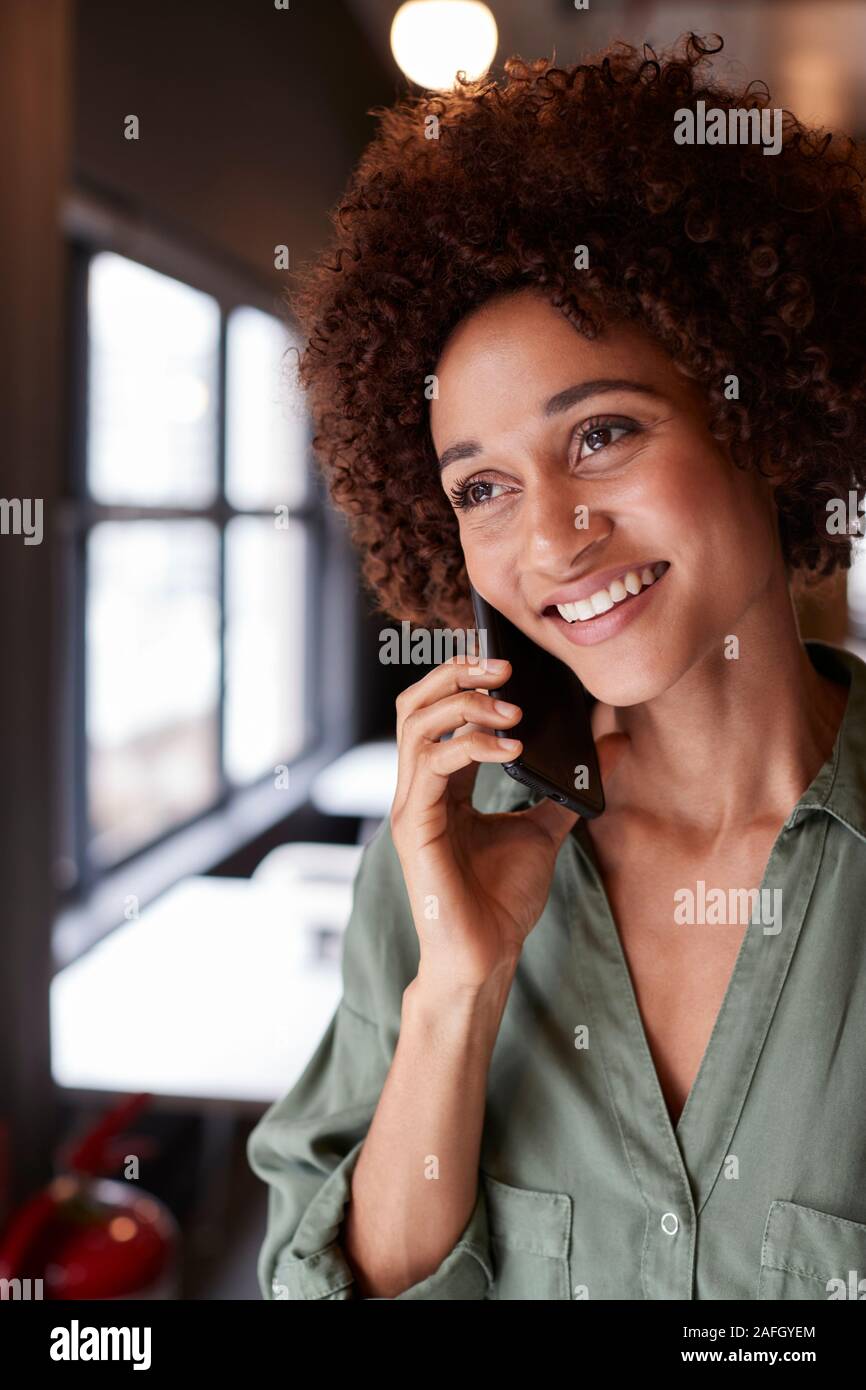 La millenaria femmina nero creative in piedi in un ufficio utilizza lo smartphone, close up, verticale Foto Stock