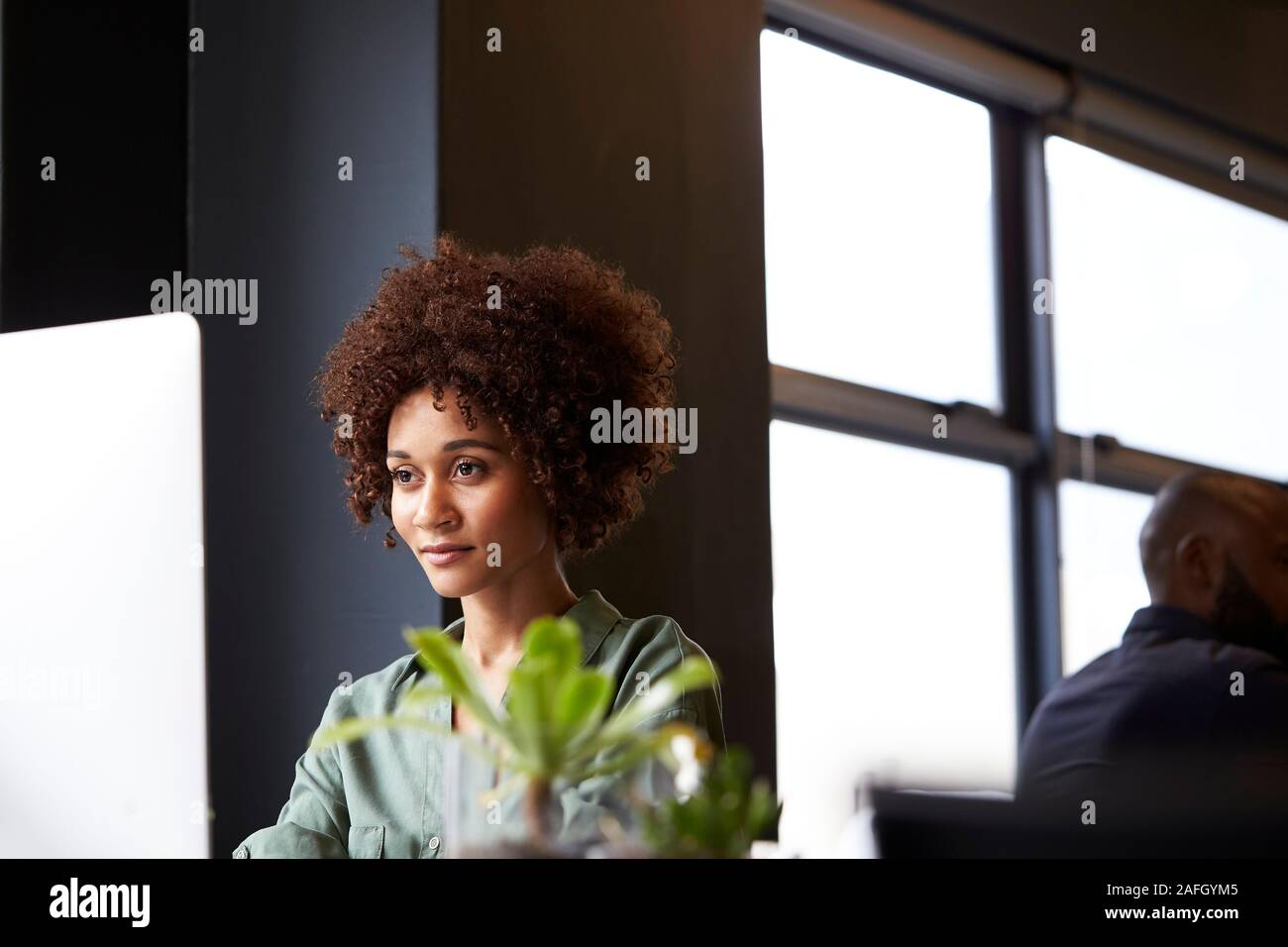 La millenaria femmina nero creative seduti ad una scrivania in un ufficio con un computer, chiudere fino Foto Stock