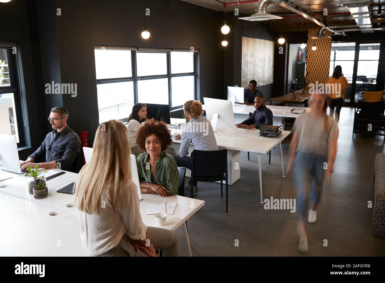 Vista in elevazione della azienda creativa colleghi impegnati a scrivanie e a piedi attraverso un ufficio occupato Foto Stock