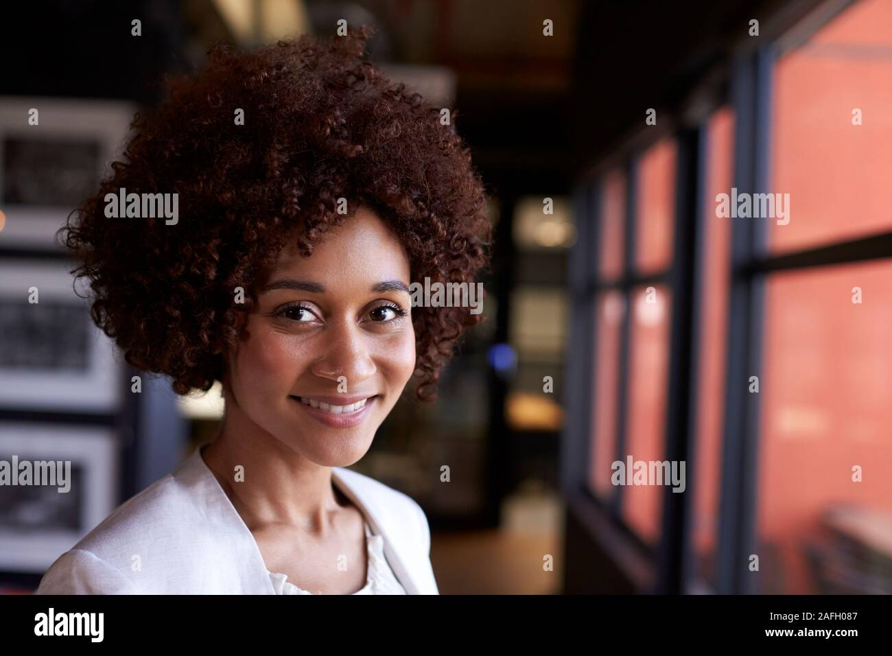 Nero millenario imprenditrice sorridere alla telecamera tramite la finestra in un ufficio, close up Foto Stock