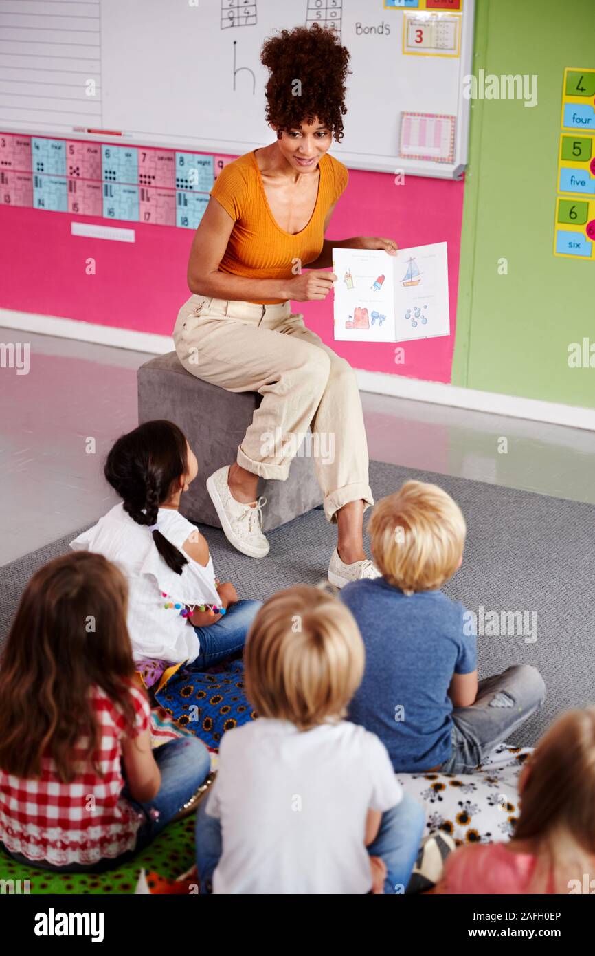 Insegnante femminile alla lettura della storia di un gruppo di alunni elementari in aula scolastica Foto Stock