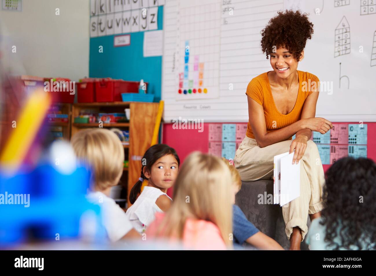 Insegnante femminile alla lettura della storia di un gruppo di alunni elementari in aula scolastica Foto Stock