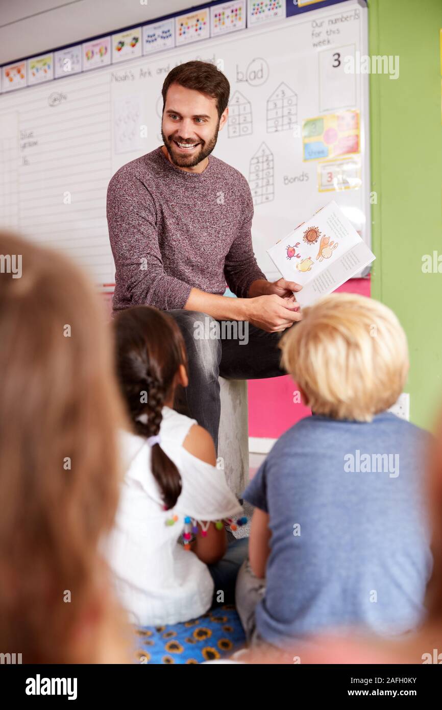 Insegnante maschio alla lettura della storia di un gruppo di alunni elementari in aula scolastica Foto Stock