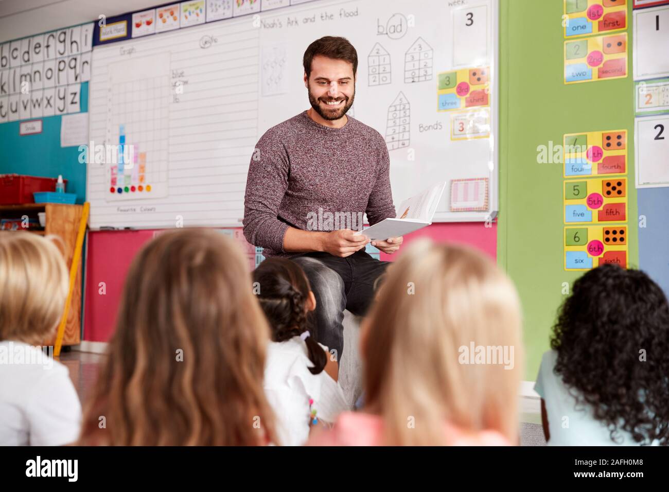 Insegnante maschio alla lettura della storia di un gruppo di alunni elementari in aula scolastica Foto Stock