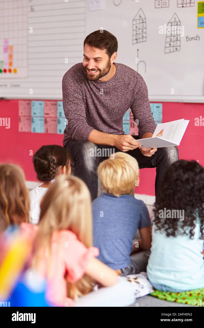Insegnante maschio alla lettura della storia di un gruppo di alunni elementari in aula scolastica Foto Stock