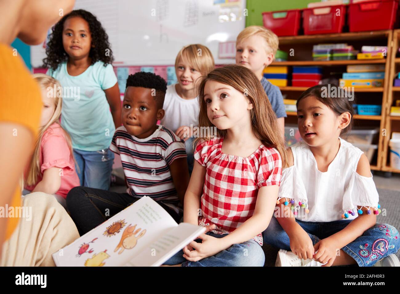 Gruppo di scuola elementare alunni seduti sul pavimento ascoltando insegnante femminile Leggi la storia Foto Stock