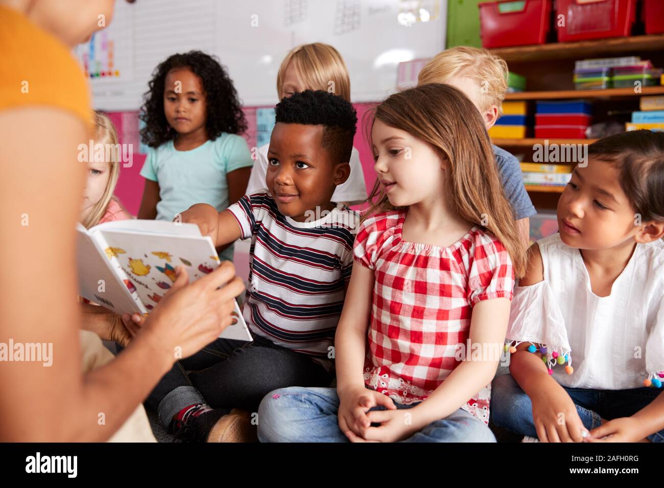 Gruppo di scuola elementare alunni seduti sul pavimento ascoltando insegnante femminile Leggi la storia Foto Stock