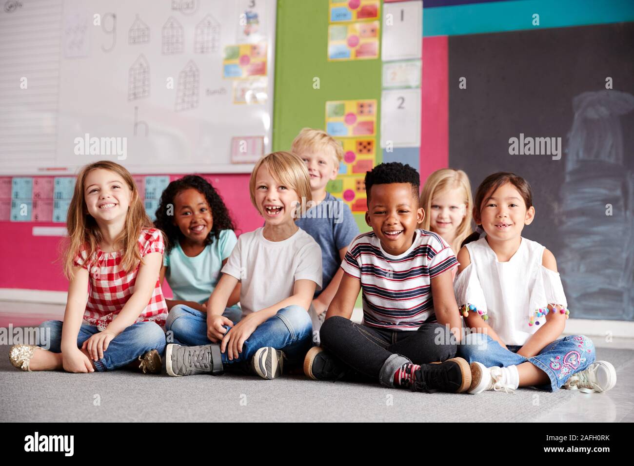 Ritratto di scuola elementare alunni seduti sul pavimento in aula Foto Stock