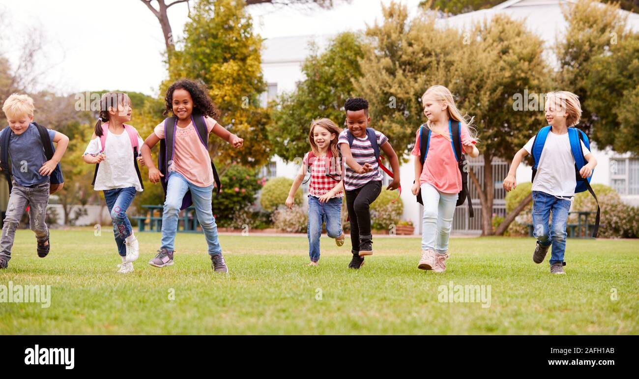 Eccitato Scuola Elementare gli alunni che attraversano il campo in corrispondenza del tempo di rottura Foto Stock
