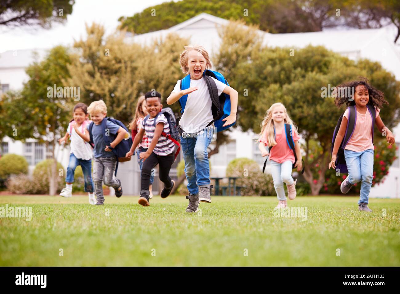 Eccitato Scuola Elementare gli alunni che attraversano il campo in corrispondenza del tempo di rottura Foto Stock