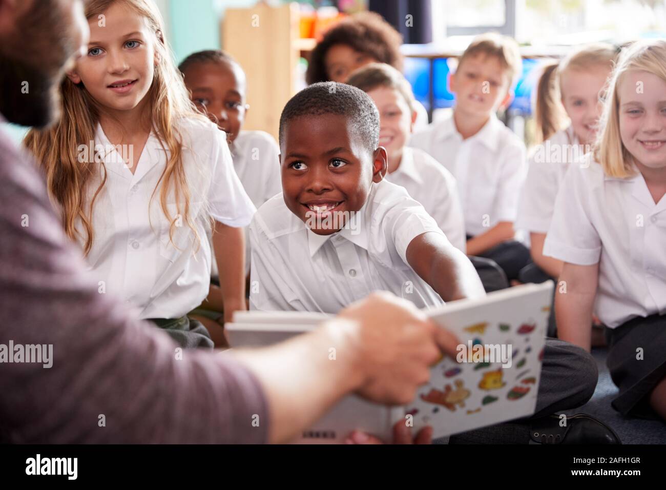 Insegnante maschio alla lettura della storia di un gruppo di alunni elementari che indossano uniformi in aula scolastica Foto Stock