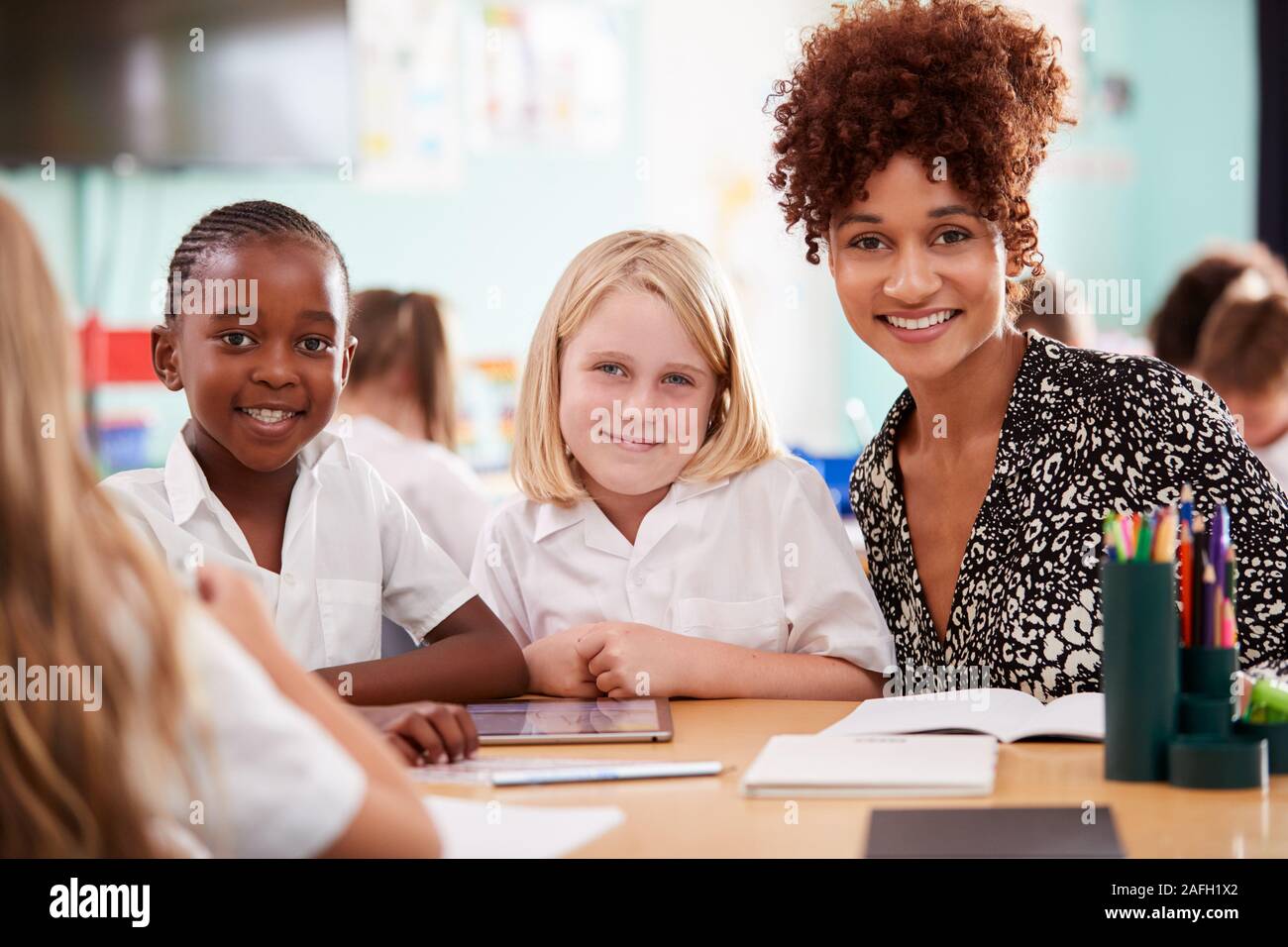 Ritratto di donna con insegnante di scuola elementare gli alunni indossano uniformi utilizzando tavoletta digitale Foto Stock