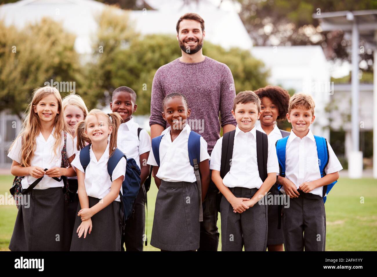 Outdoor ritratto della scuola elementare di alunni con insegnante indossano uniformi in piedi sul campo da gioco Foto Stock