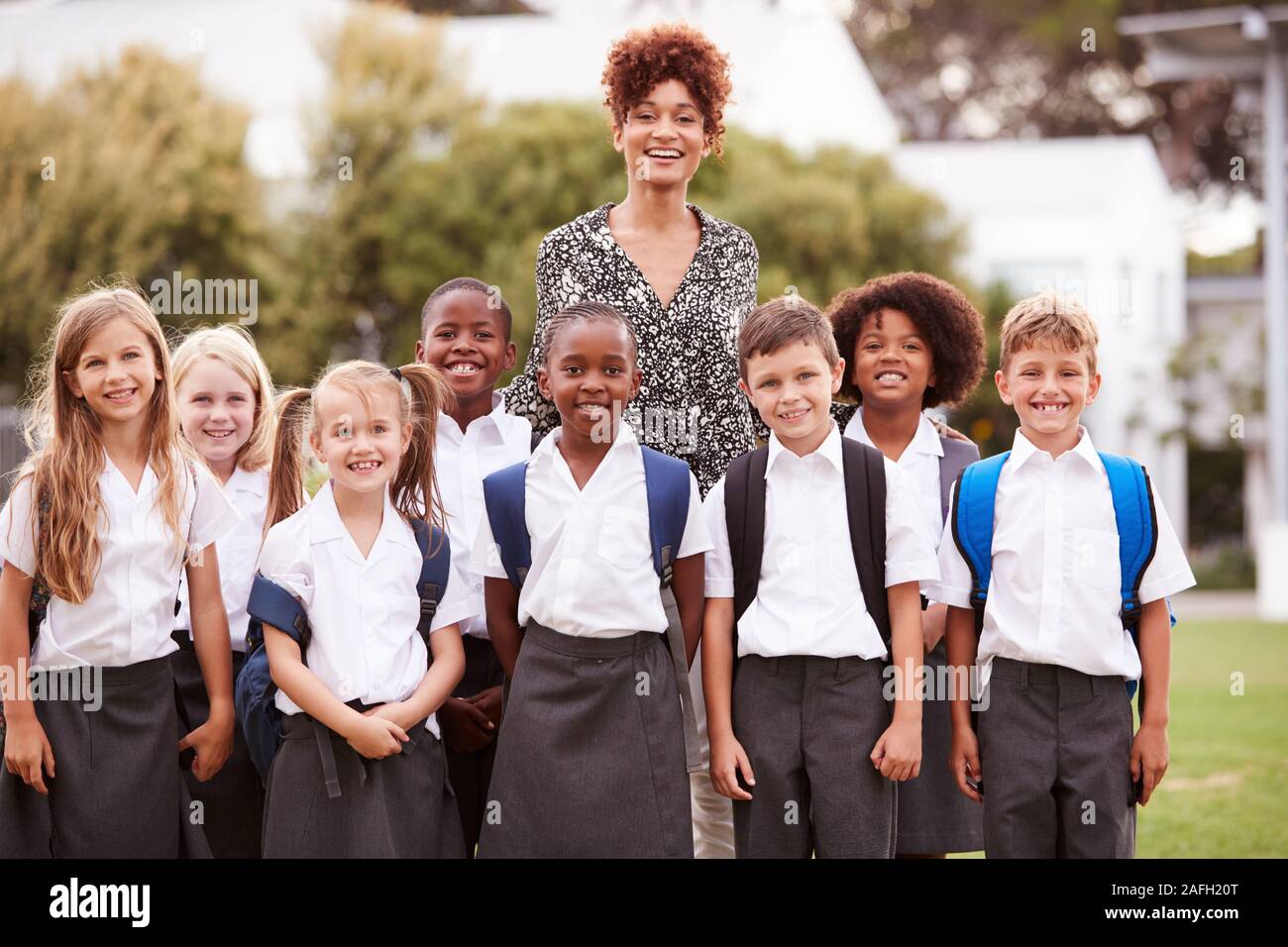 Outdoor ritratto della scuola elementare di alunni con insegnante indossano uniformi in piedi sul campo da gioco Foto Stock