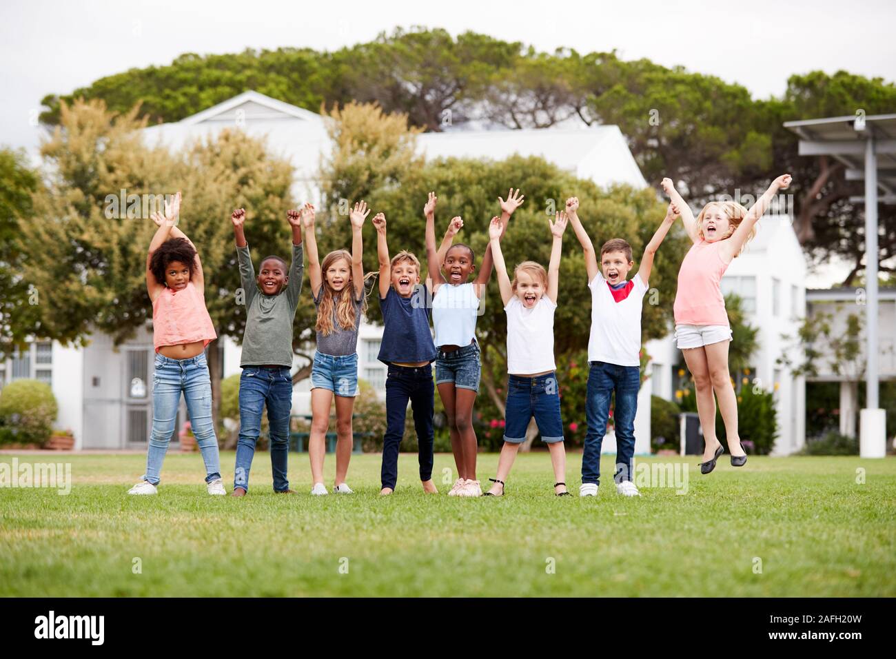 Gruppo di entusiasti della scuola elementare di alunni in piedi sul campo da gioco al momento di rottura con le braccia sollevate Foto Stock
