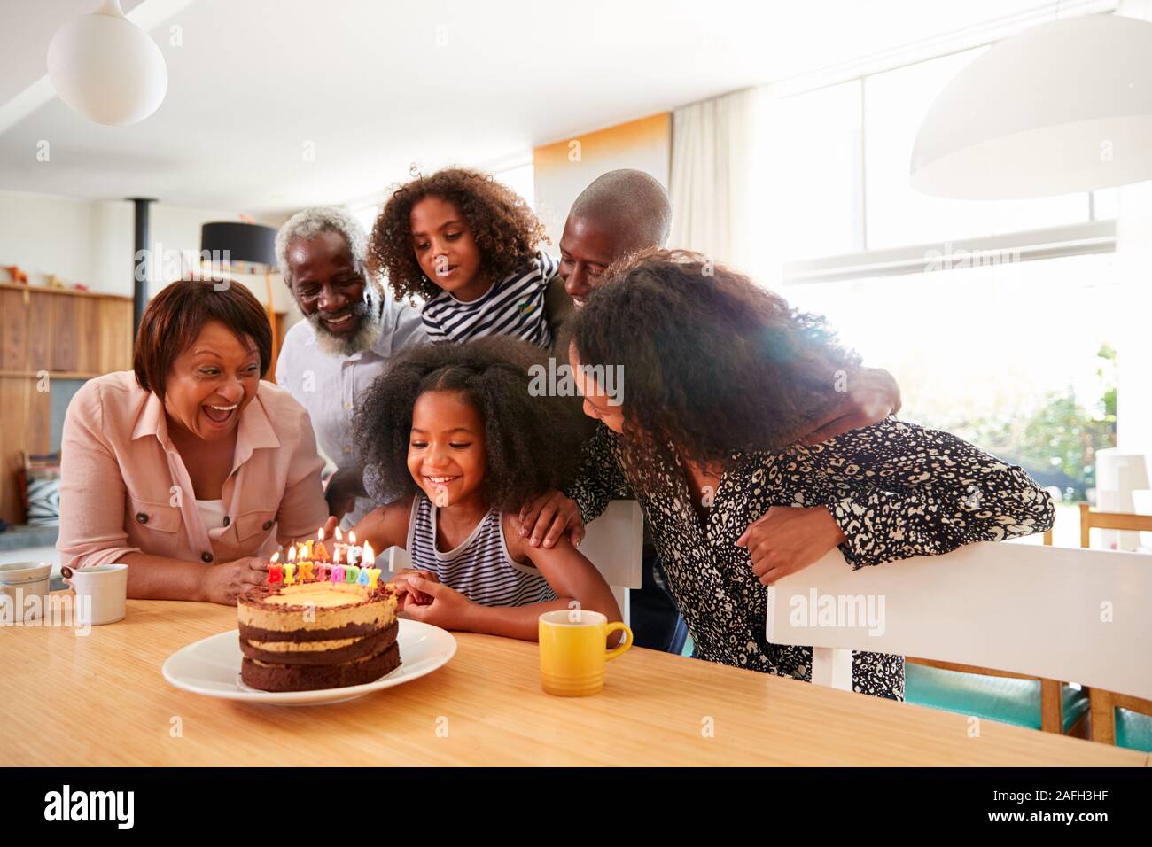 Famiglia Multi-Generation celebrando nipoti compleanno a casa con torta e candele Foto Stock
