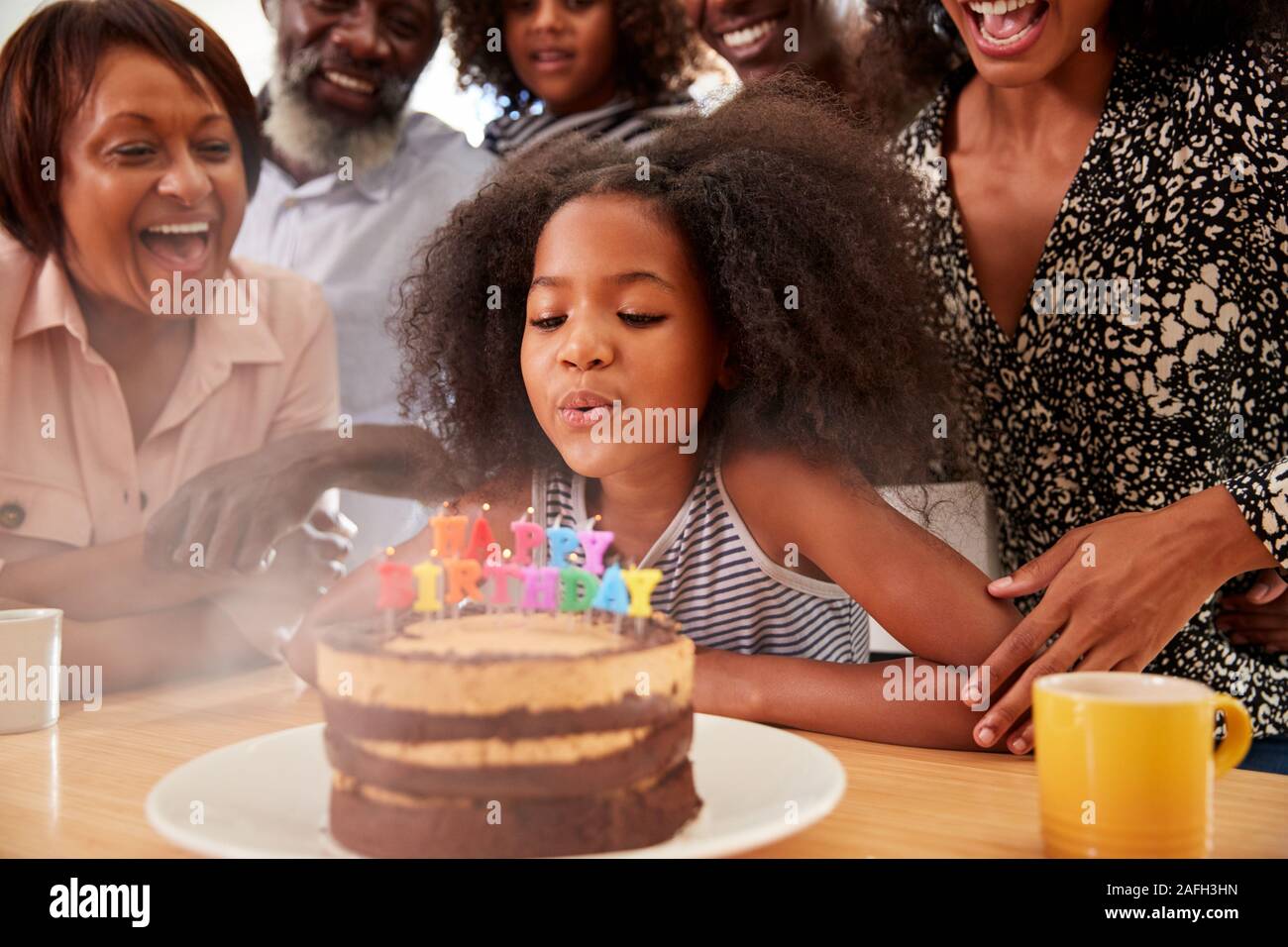 Famiglia Multi-Generation celebrando nipoti compleanno a casa con torta e candele Foto Stock