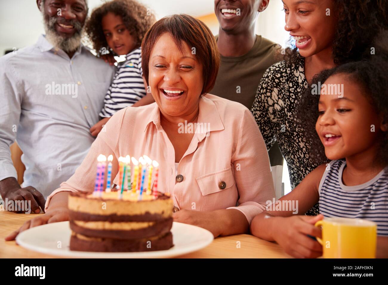Famiglia Multi-Generation celebrando nonne compleanno a casa con torta e candele Foto Stock