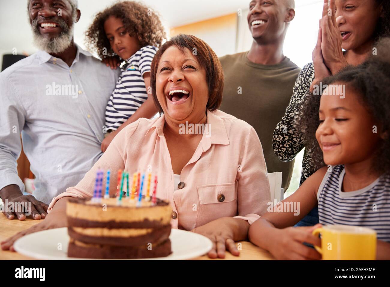 Famiglia Multi-Generation celebrando nonne compleanno a casa con torta e candele Foto Stock