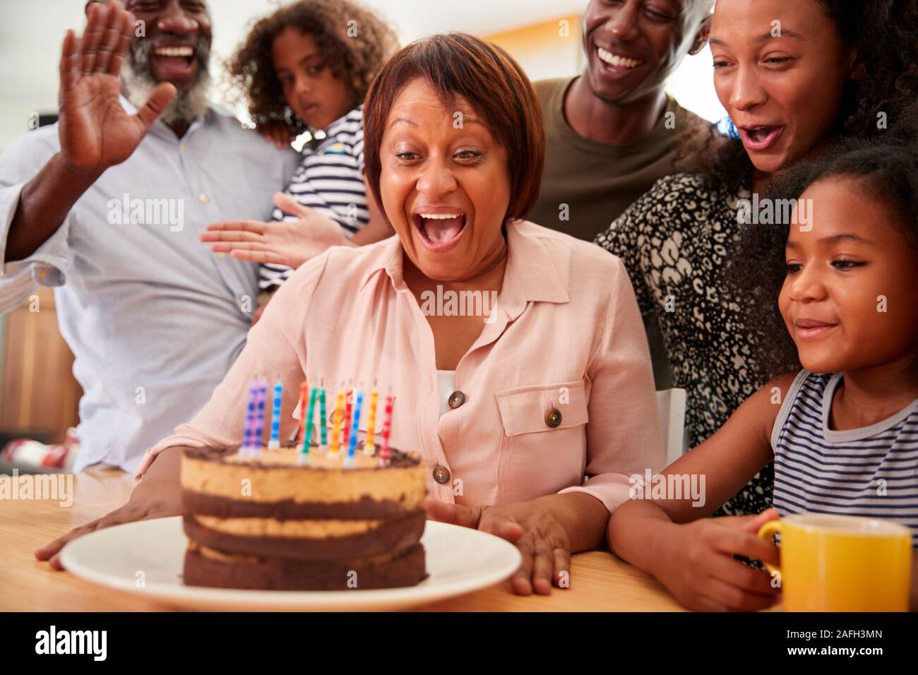 Famiglia Multi-Generation celebrando nonne compleanno a casa con torta e candele Foto Stock
