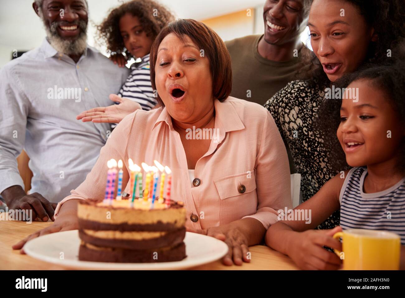 Famiglia Multi-Generation celebrando nonne compleanno a casa con torta e candele Foto Stock