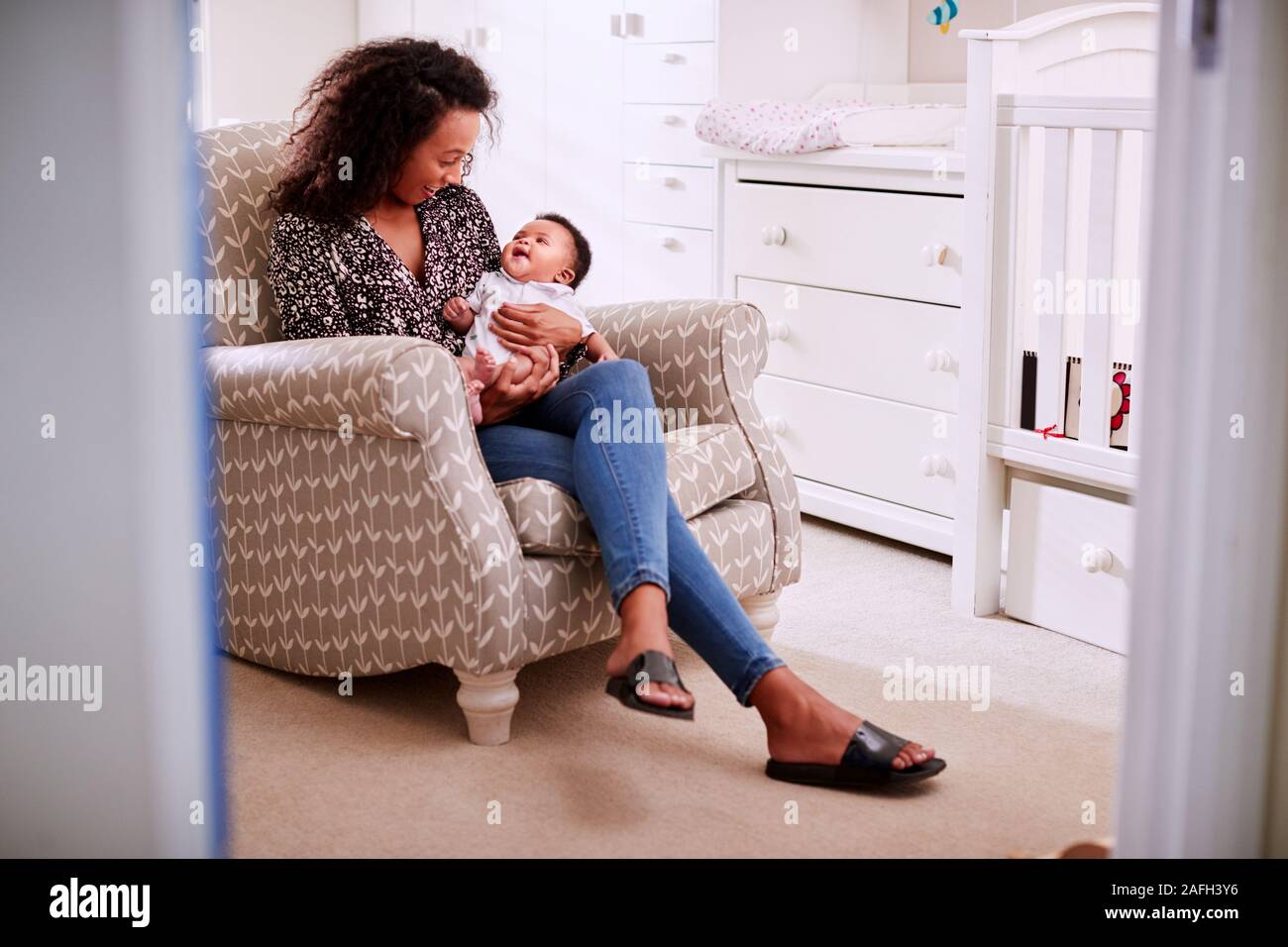 Amorevole Madre seduto nella sedia Cuddling Baby figlio in un asilo nido a casa Foto Stock