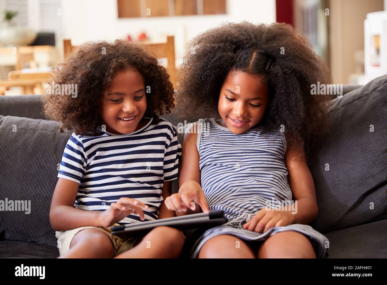 Fratello e Sorella seduti sul divano di casa a giocare con tavoletta digitale Foto Stock