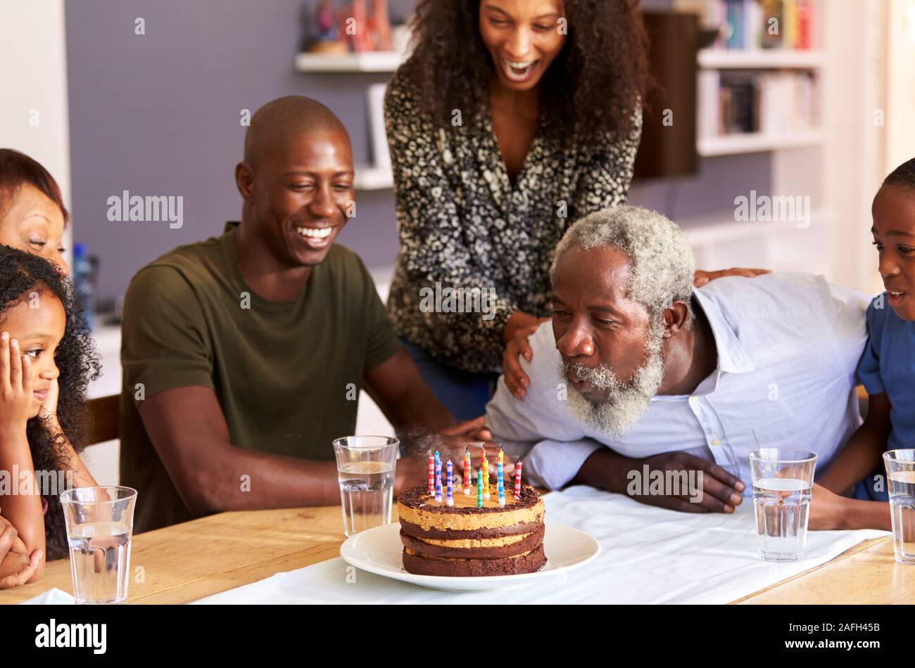 Famiglia Multi-Generation celebrando i nonni compleanno a casa con torta e candele Foto Stock