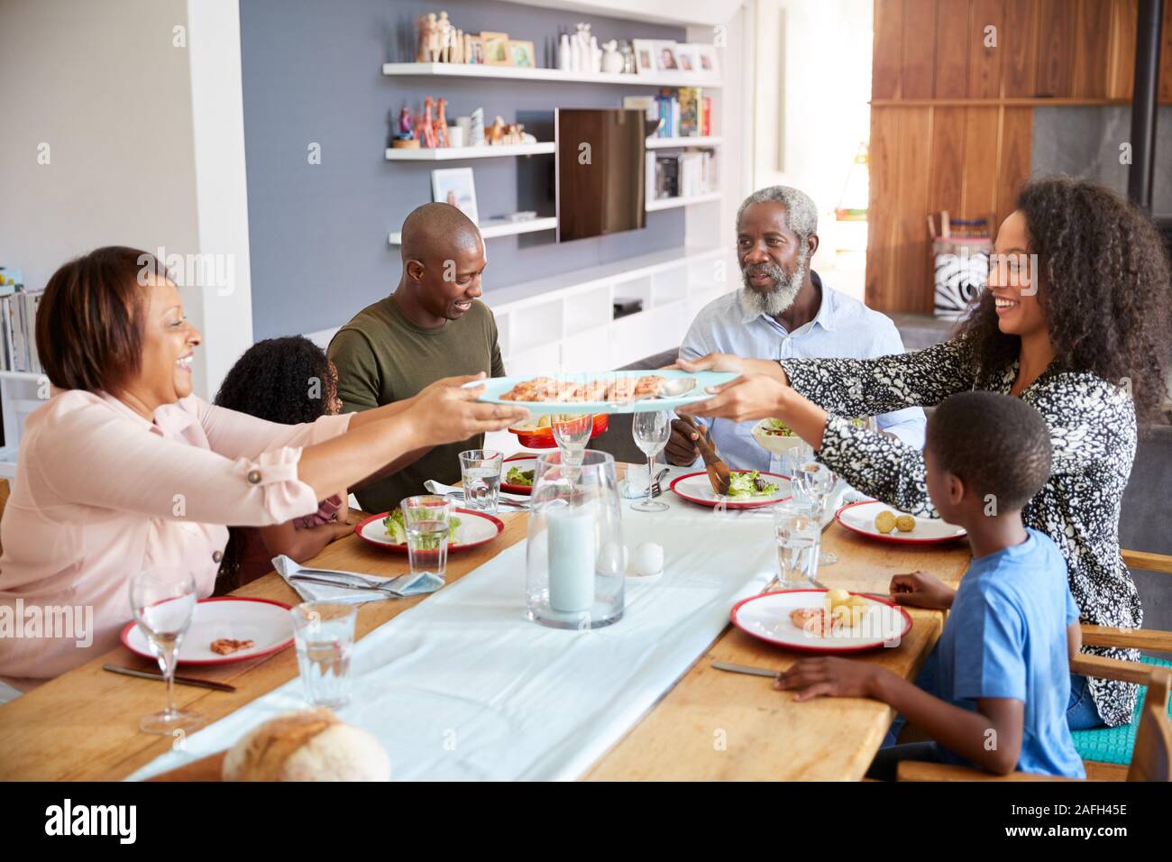 Famiglia Multi-Generation seduti attorno al tavolo di gioco a casa godendo di pasto insieme Foto Stock