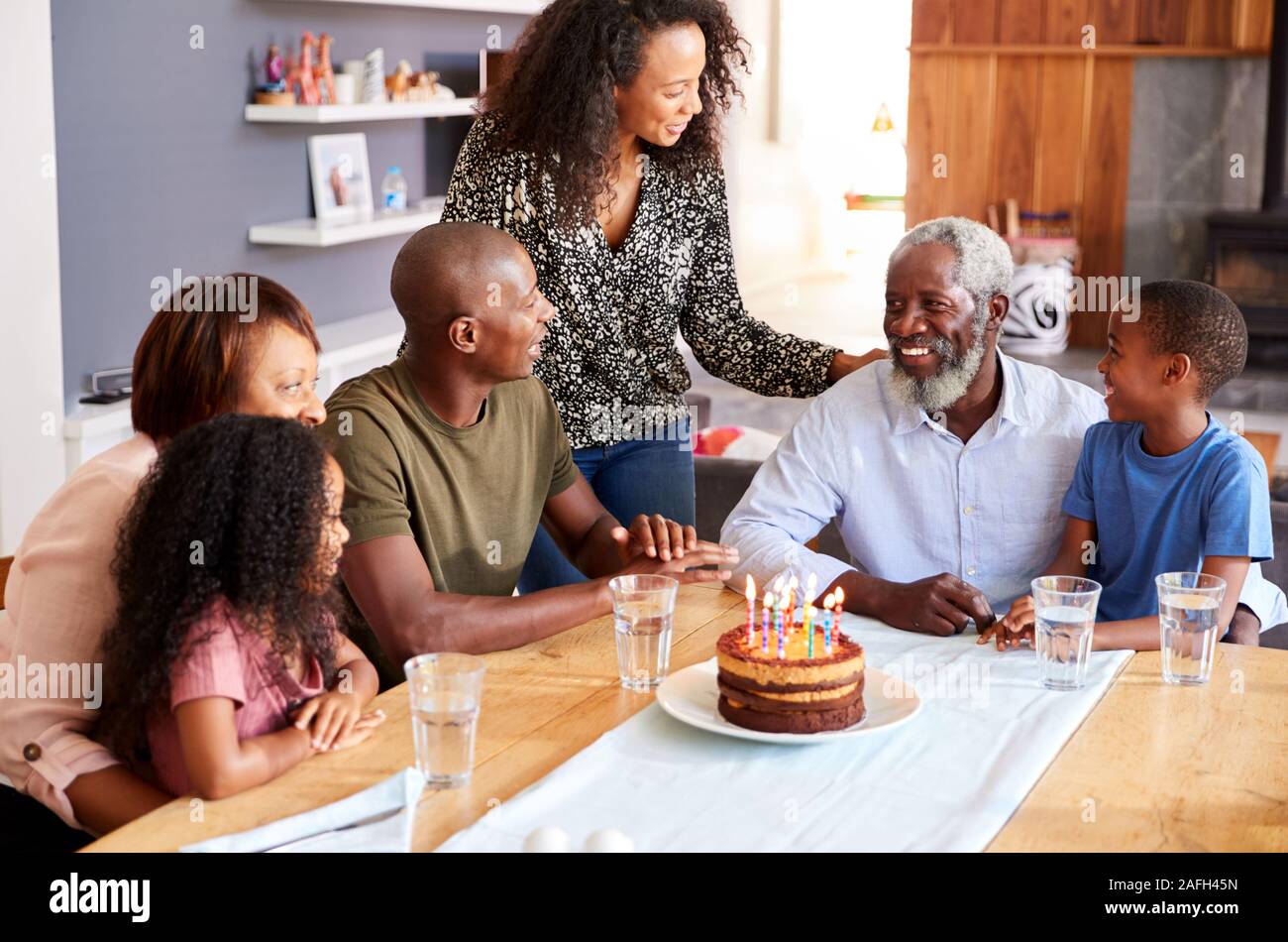 Famiglia Multi-Generation celebrando i nonni compleanno a casa con torta e candele Foto Stock