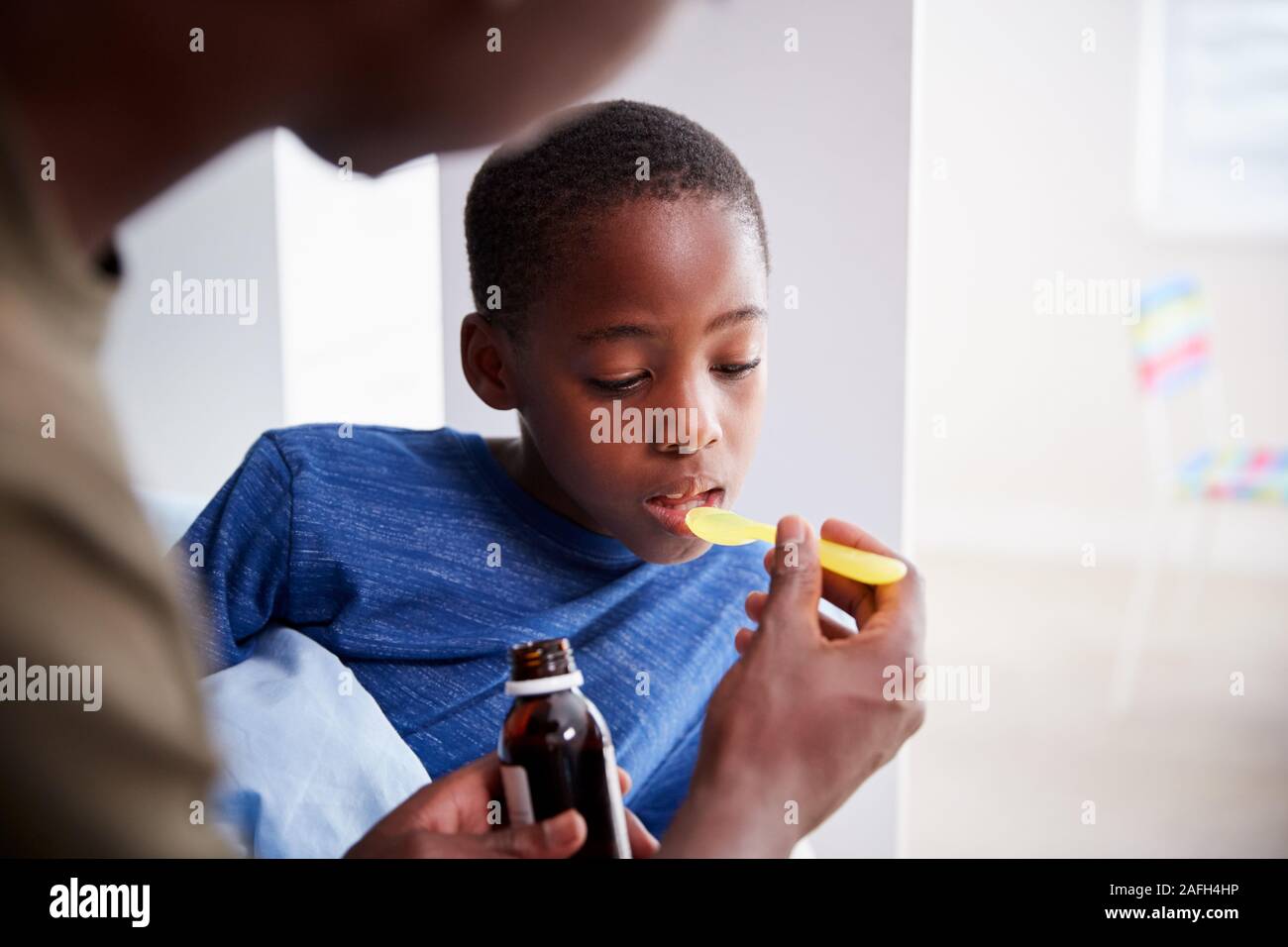 Padre dando figlio malato a letto malato medicina da bottiglia Foto Stock