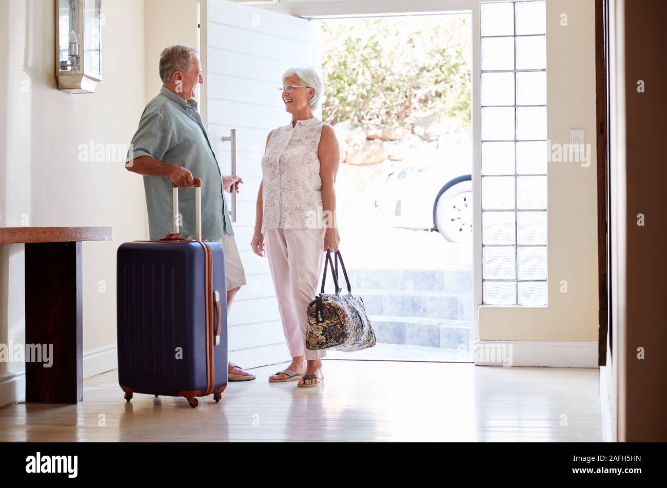 Coppia senior in piedi dalla Porta anteriore con la valigia in procinto di partire per le vacanze Foto Stock